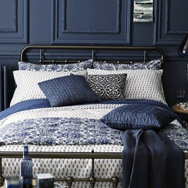 Classic navy and grey bedroom featuring patterned bedding, elegant wall paneling, and cozy textured accents.
