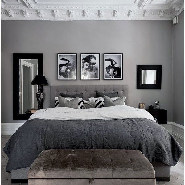 Modern bedroom with a grey color scheme, featuring a large bed, artwork above, and a bench at the foot of the bed