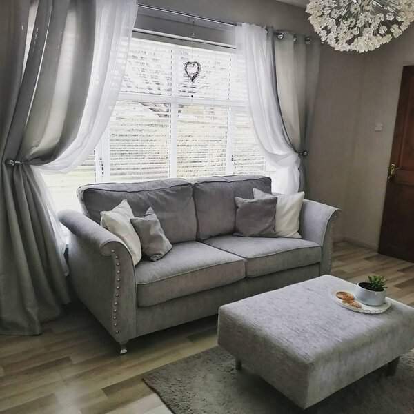 Grey and white living room with elegant drapes, plush sofa, and a cozy ottoman.
