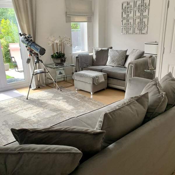 Grey and white living room with plush sofas, decorative wall art, and a telescope by the window.