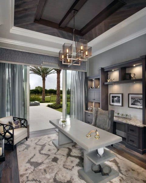 Luxury home office with a modern grey desk, shelving, chandelier, and garden view.