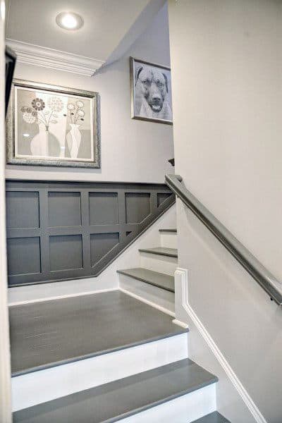 A sleek staircase with gray wainscoting and photo frames adorning the walls