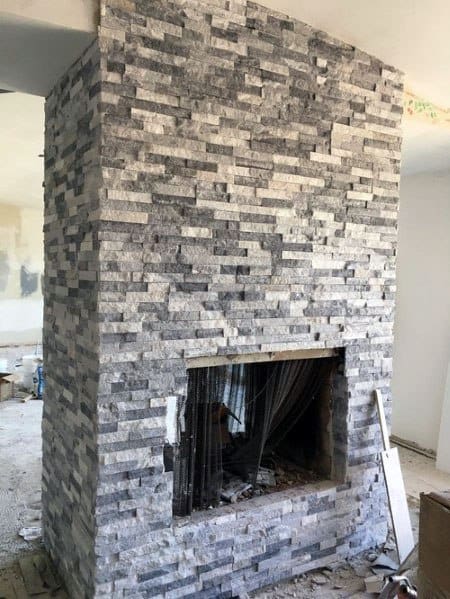 Unfinished grey and white stacked stone fireplace showcasing a unique and modern design in progress
