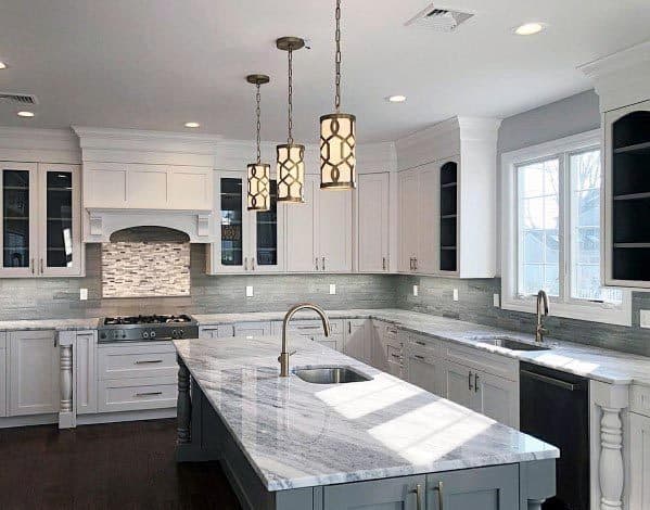 Modern kitchen with white cabinets, grey backsplash, marble countertops, and pendant lights.