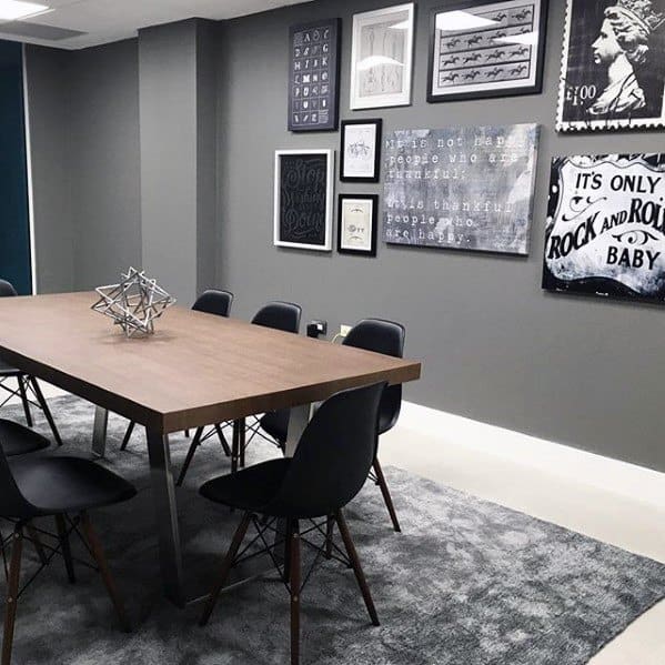 Framed black and white wall art in a modern office space with a wooden table and black chairs.