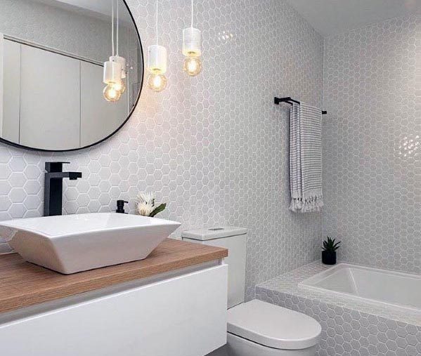 A chic grey bathroom with honeycomb tiles, a wooden vanity, a vessel sink, and modern pendant lighting.
