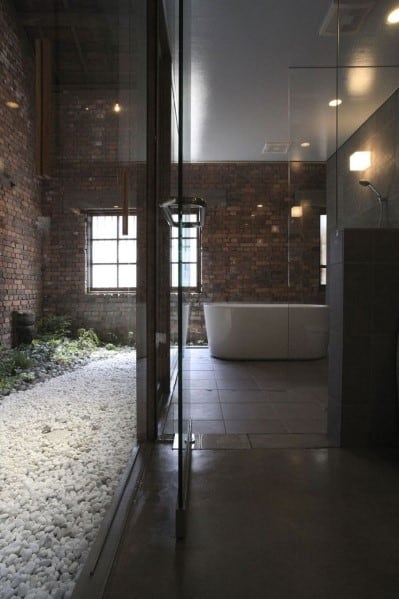 Industrial-style bathroom with brick walls, a bathtub, and a glass-walled shower area
