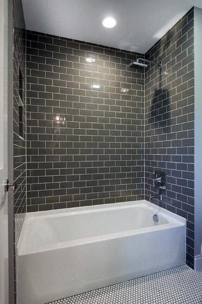 A bathroom design featuring glossy gray subway tiles on the wall, a white bathtub, and patterned white-and-black floor tiles for a sleek modern look.