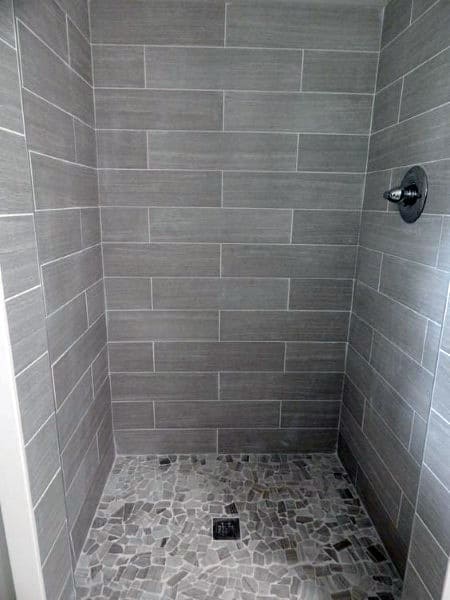 Grey travertine tile shower with mosaic pebble floor and matte black showerhead.