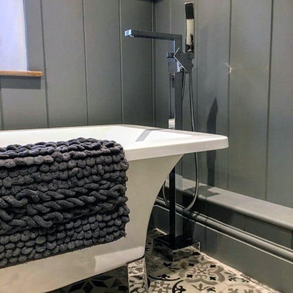 Rustic grey bathroom with wood panel walls, a freestanding white bathtub, and patterned tile flooring.