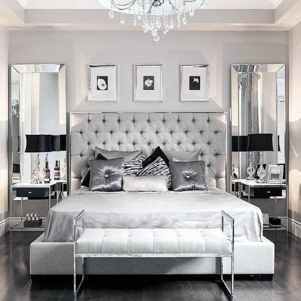 Elegant bedroom with a plush, tufted bed, grey silver bench, mirrored side tables, and chandelier