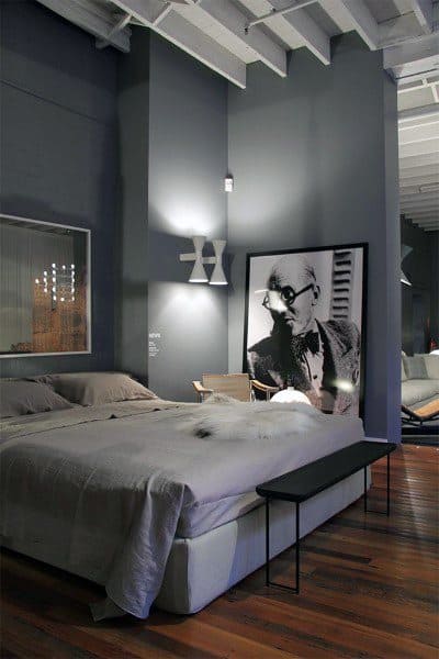 Modern bedroom with dark grey walls, double bed, abstract art, and wooden floor; subtle lighting creates a cozy ambiance