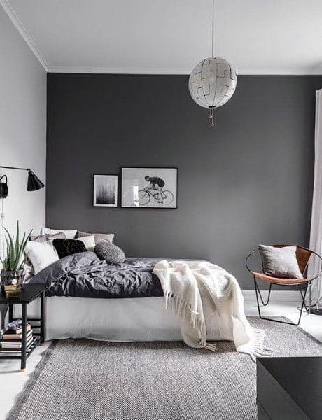 Modern bedroom with grey accent wall, bed with gray and white bedding, chair, and minimal decor