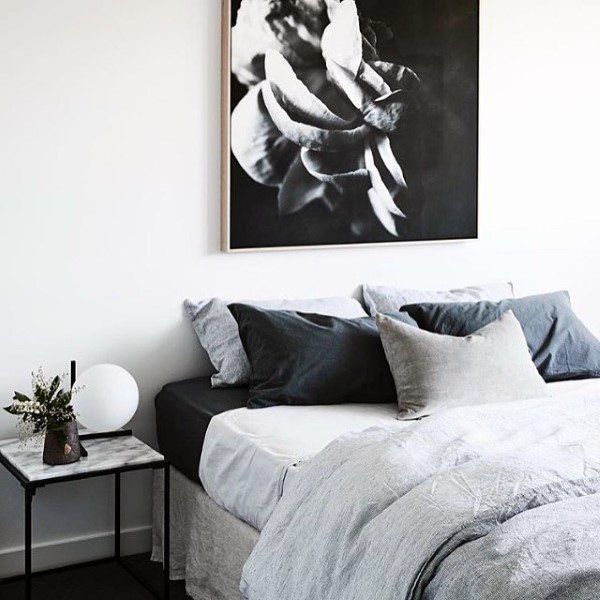 Minimalist bedroom with a grey monochrome floral painting, neatly arranged pillows, and a small side table with a vase