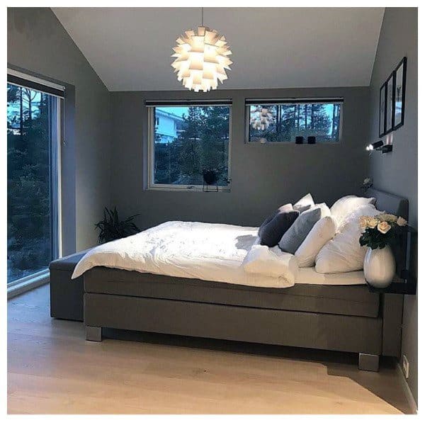 Modern bedroom with a large grey bed, white bedding, a pendant light, and windows showing an outdoor view