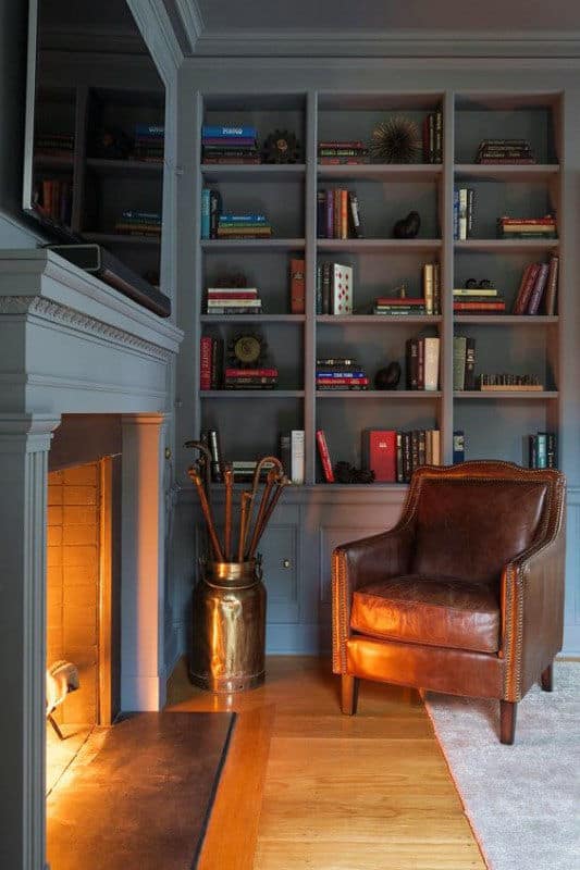 Cozy room with a library vibe, featuring a brown leather armchair, lit fireplace, and bookshelves with books and ornaments