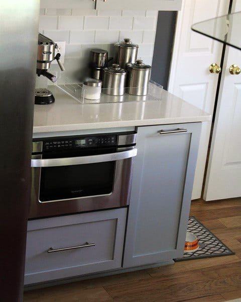 Compact coffee bar with grey cabinets, white countertop, espresso machine, and stainless steel canisters.
