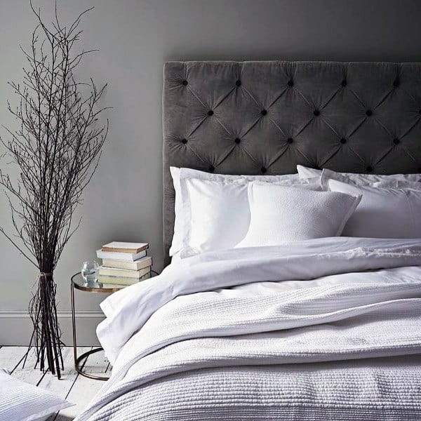 Cozy bedroom with a tufted headboard, white bedding, a stack of books, and a decorative branch in a vase
