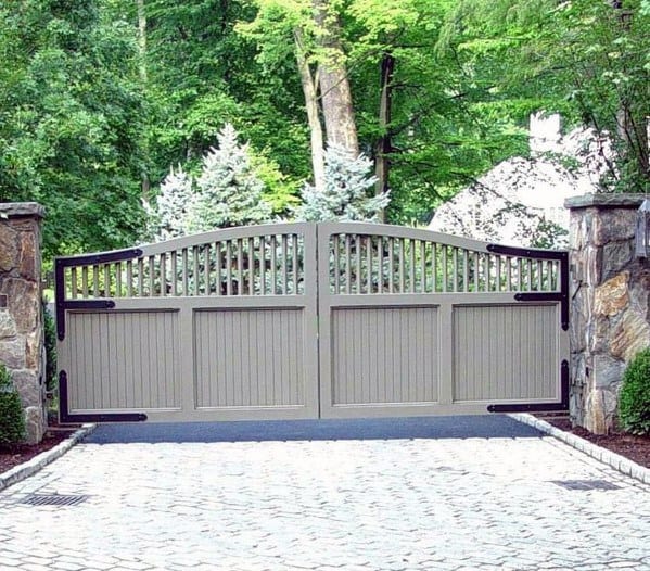Gray wooden driveway gate with arched top and vertical slats, accented by stone pillars.