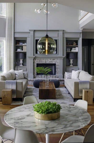 Spacious living room with gray built-in bookcases, brick fireplace, marble dining table, and modern gold pendant light