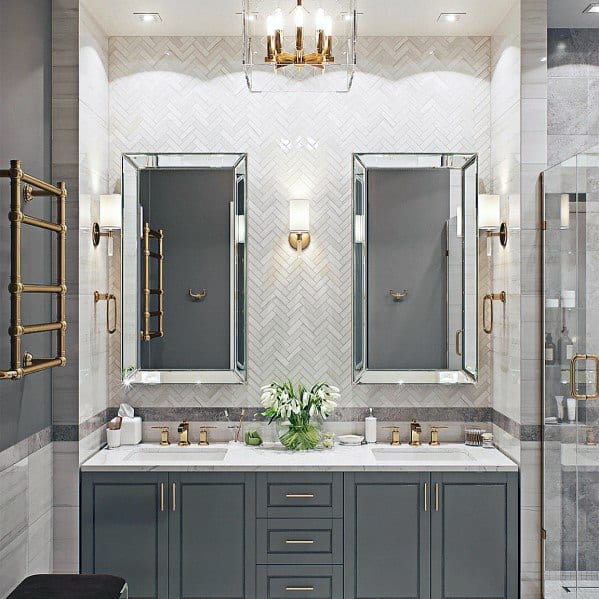 Elegant grey double vanity with mirrored cabinets, gold fixtures, and herringbone backsplash.