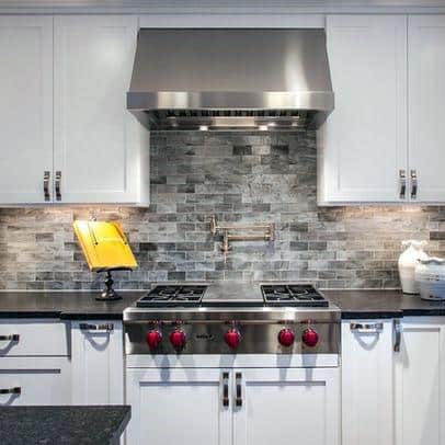 Modern kitchen with white cabinets, a grey stone backsplash, stainless steel appliances, and bold red stove knobs