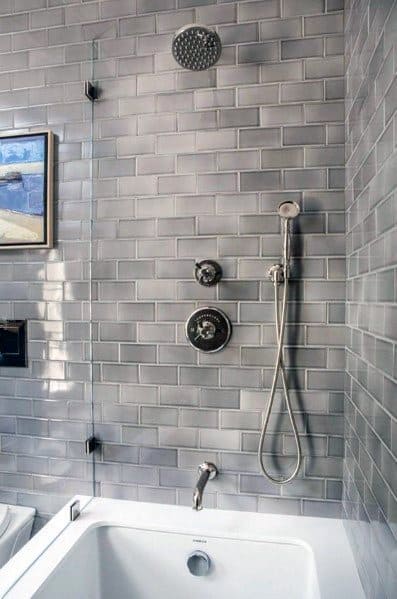 Modern bathroom with gray beveled subway tiles, showerhead, and white bathtub.