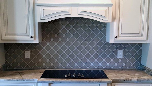 The grey backsplash with a trellis pattern complements the white cabinetry for an elegant, cohesive look.