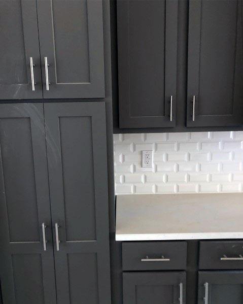 Dark grey kitchen cabinets with white countertops and a textured white backsplash.