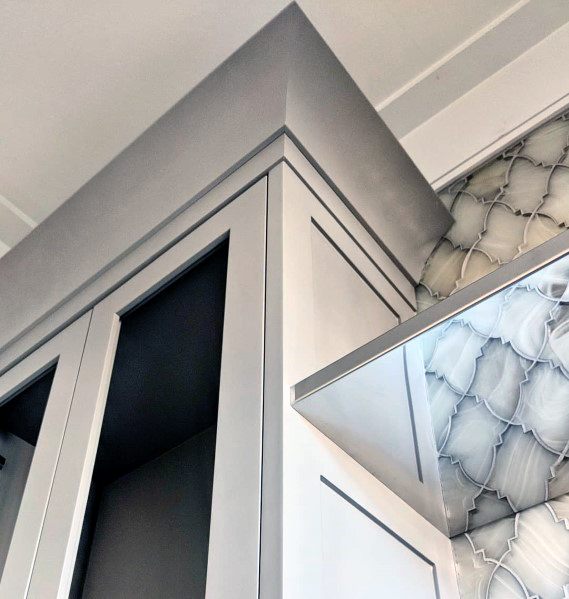 A modern kitchen with sleek grey cabinetry, sharp crown molding, and a stylish backsplash, creating a clean, contemporary look