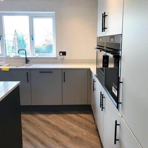 Modern grey kitchen with black hardware, built-in appliances, and wood-style flooring.