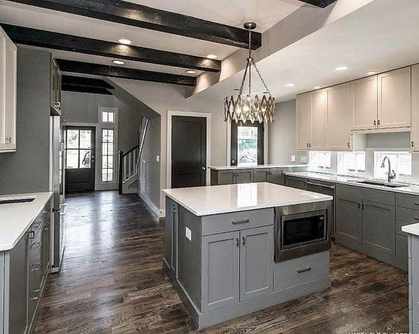 Grey kitchen with central island, exposed beams, hardwood flooring, and chandelier lighting.