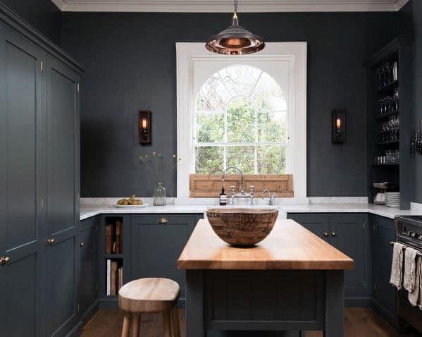 Dark grey kitchen with wooden island, copper pendant light, and large arched window.