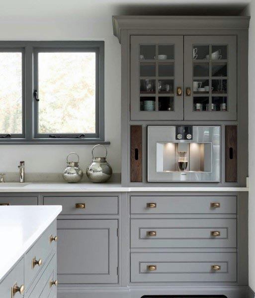 Grey kitchen with glass-front cabinets, built-in coffee machine, and brass hardware.