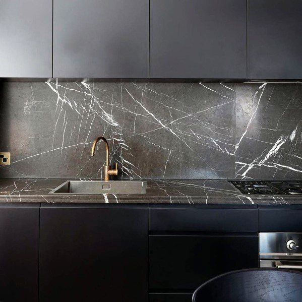Modern kitchen featuring sleek black cabinets, a dark grey marble backsplash with white veining, and a gold faucet