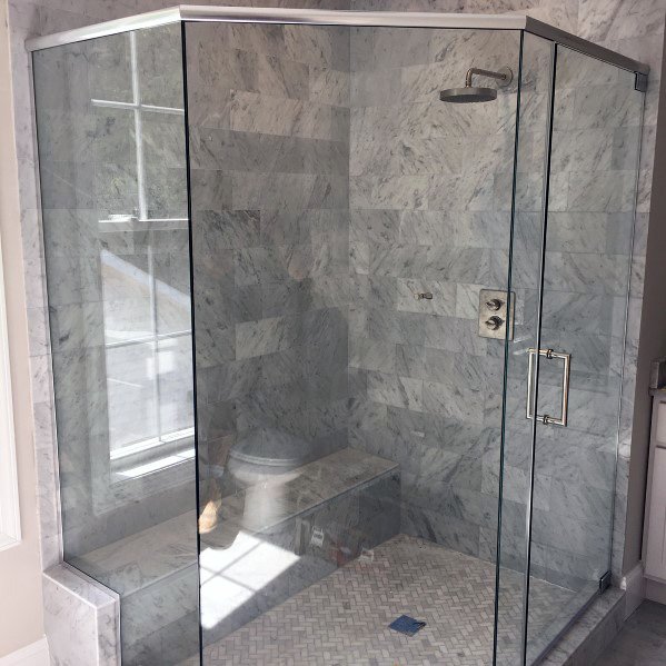 Corner glass-enclosed shower with marble tiles and a built-in bench in a bright bathroom