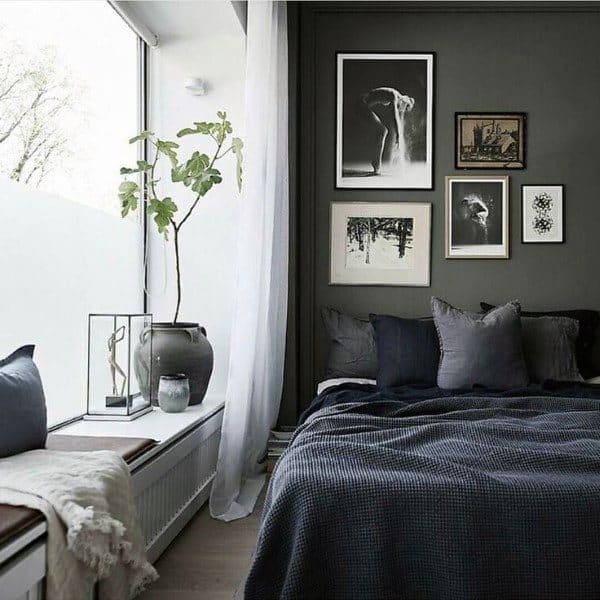 Minimalist bedroom with dark walls, framed art, a large window, a plant, and a cozy bed with grey bedding