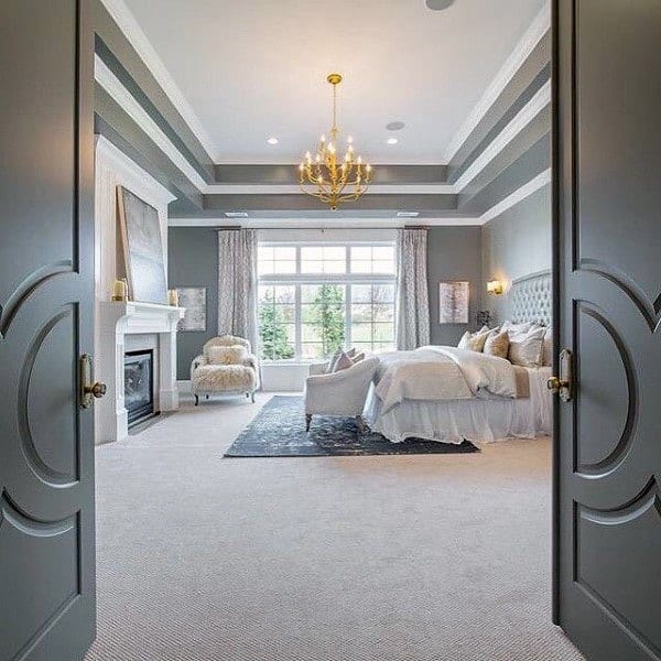 Luxurious bedroom with chandelier, fireplace, elegant furnishings, and large window view; double doors open inward