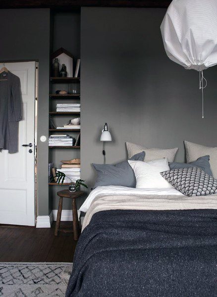 Cozy bedroom with grey walls, white and gray bedding, a wall lamp, decor shelf, and a white pendant light