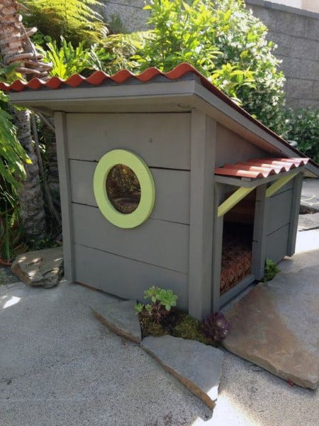A modern gray doghouse with a circular window, slanted roof, and cozy space for your dog