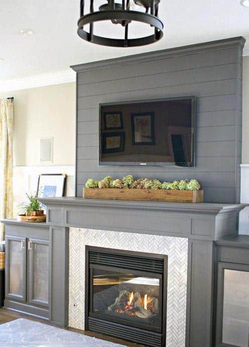 Gray shiplap fireplace with a matching wood mantel, herringbone tile surround, and mounted TV.