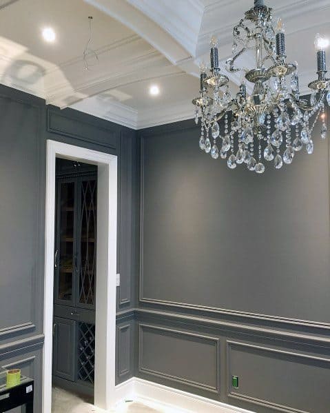 Gray dining room with decorative paneling, white ceiling, and crystal chandelier.