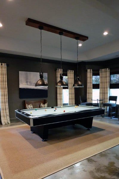 Modern billiard room with grey walls, concrete floors, and a pool table under pendant lights.