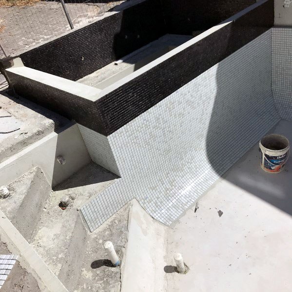 Unfinished pool with white mosaic tiles and a sleek black waterline accent under construction.