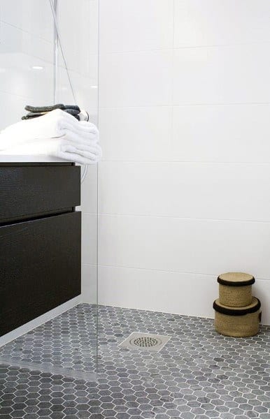 Bathroom with small gray hexagonal floor tiles, glass shower, and white tiled walls.