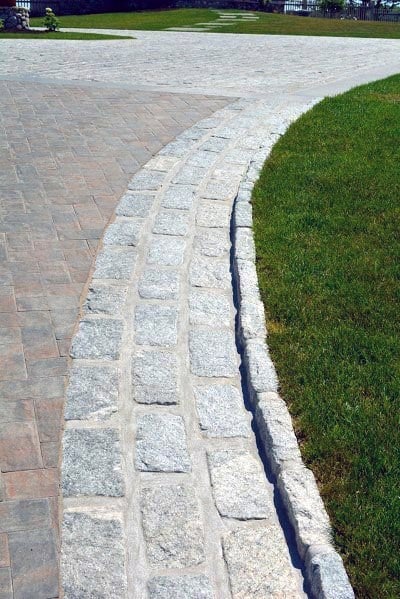 A neatly paved driveway with a curved gray stone border, complementing the green lawn and adding structure to the landscape