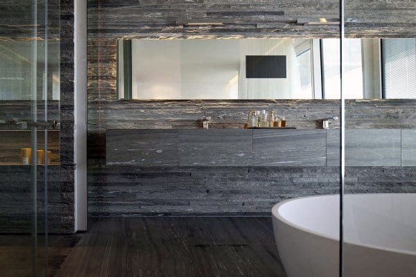 Modern bathroom with stone walls, large mirror, and a freestanding bathtub in foreground