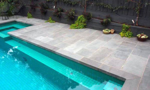 Modern pool with green mosaic tiles and surrounding grey stone patio, complemented by a vertical garden.