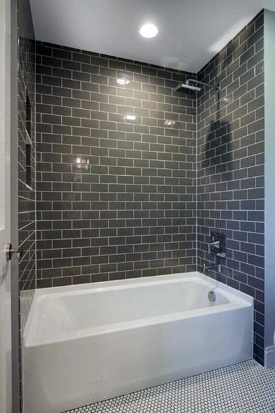 White bathtub with dark gray beveled subway tile wall and patterned floor tiles.