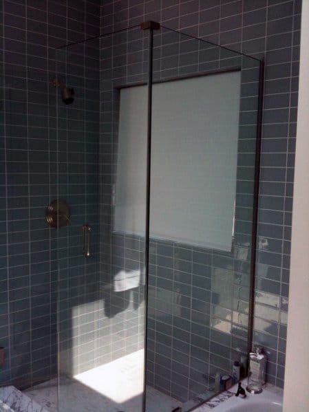 Modern corner shower with glass door and gray tile walls, featuring closed white window blind inside